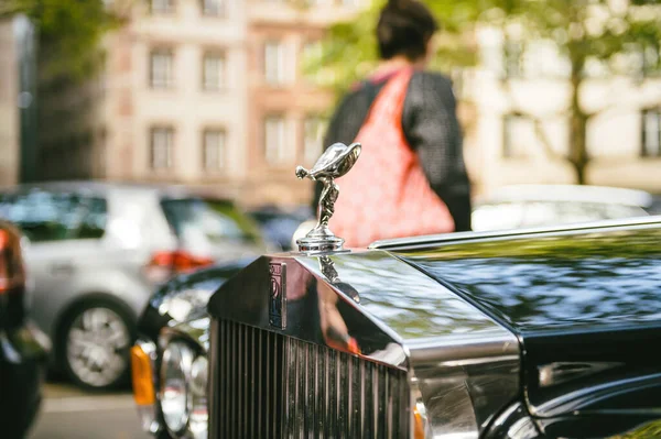 Primer plano del emblema de la dama voladora Rolls Royce en el radiador de limusina de lujo con mujer peatonal en el fondo —  Fotos de Stock