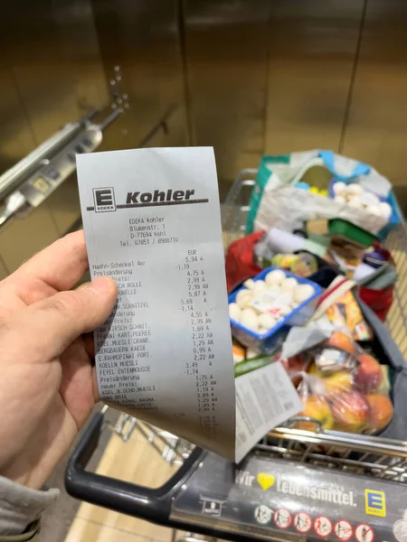 POV mão macho segurando recibo de supermercado de Edeka Supermercado no elevador de um centro comercial olhando para os preços dos produtos no carrinho — Fotografia de Stock
