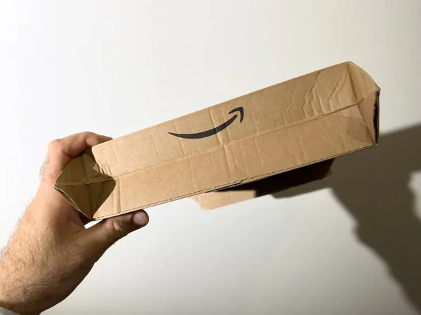 POV male hand holding against wall hero object shot of Amazon Prime logotype on the new cardboard box drive — Foto de Stock