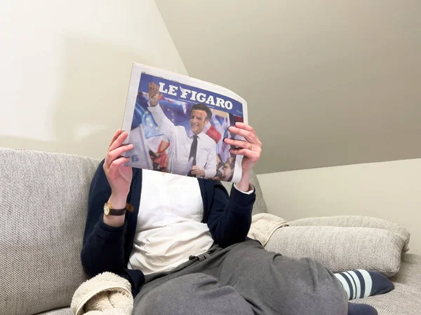 Mujer leyendo en un acogedor sofá el último periódico Le Figaro, cubrir con Frances presidente titular Emmanuel Macron después de vencer a Marine Le Pen por un segundo mandato de cinco años —  Fotos de Stock