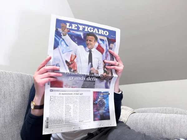 Woman reading on a cozy couch latest Le Figaro newspaper, cover with Frances incumbent president Emmanuel Macron after beating Marine Le Pen for a second five-year term — Zdjęcie stockowe