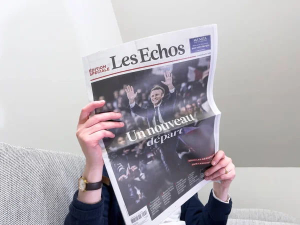 Woman reading on a cozy couch latest Les Echos newspaper, cover with Frances incumbent president Emmanuel Macron after beating Marine Le Pen for a second five-year term — Foto de Stock