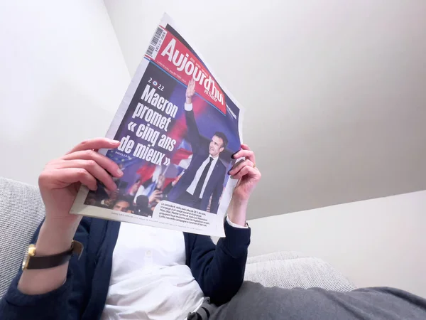 Woman reading on a cozy couch latest Aujordhui newspaper, cover with Frances incumbent president Emmanuel Macron after beating Marine Le Pen for a second five-year term — Stockfoto
