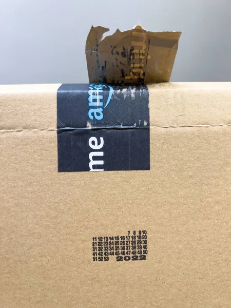 POV mano masculina sosteniendo nuevo paquete corrugado ecológico con el logotipo de comercio electrónico de compras en línea de Amazon Prime en la banda escocesa y 2022 año de producción del material reciclado —  Fotos de Stock