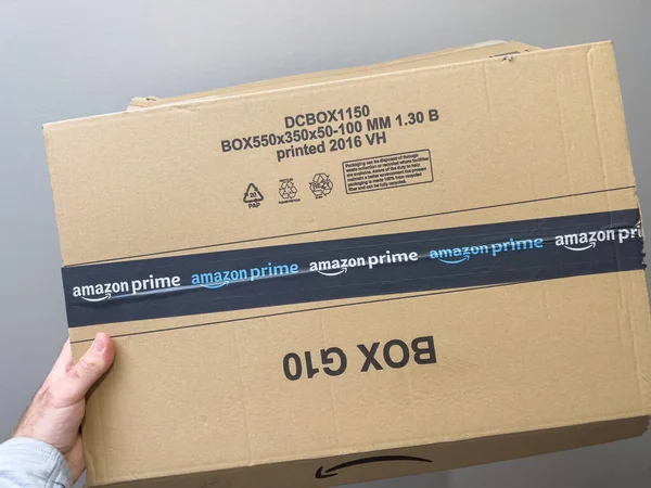 POV mano masculina sosteniendo nuevo paquete corrugado respetuoso con el medio ambiente con Amazon Prime comercio electrónico logotipo — Foto de Stock