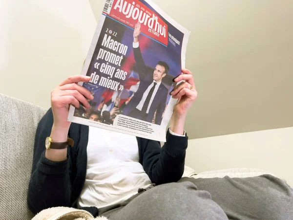 Kvinna läser på en mysig soffa senaste Aujordhui tidningen, täcka med Frances sittande president Emmanuel Macron efter att ha slagit Marine Le Pen för en andra femårsperiod — Stockfoto