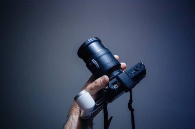 Basel, İsviçre - 19 Mayıs 2022: V1 aynasız Nikon biçimi için yeni Nikon 1 NIKOR 10-100mm f 4.5-5.6 VR kamera lensi mavi teknoloji arka planına karşı POv erkek eli