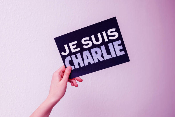 POV woman hand holding Je Suis Charlie in French language translation I Am Charlie card on gray background