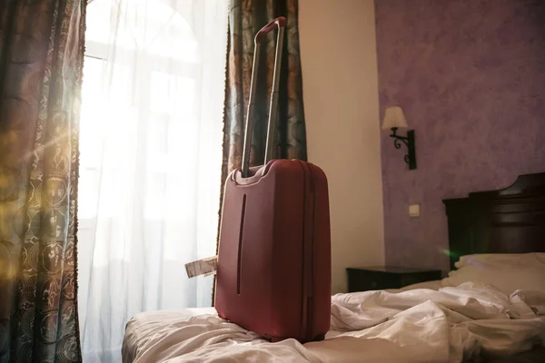 Interior of bedroom with messy bed and red hand luggage on the luxury satin linen beddings