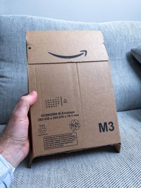 Paris, France - Jan 27, 2022: Amazon Prime cardboard package with M3 signage - recycled cardboard box on teh couch background - blue color cast