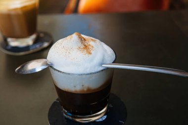 Close-up view of delicious cappuccino in glass with long spoon over the milky foam