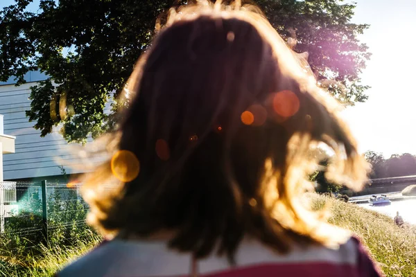 Rear view of carefree woman with sunlight flare over her hair rear view unrecognizable person