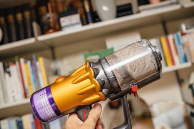 Paris, France - July 13, 2022: POV male hand holding new cordless vacuum cleaner by Dyson V12 with filled bin multiple dust particle, hair and other debris found in house