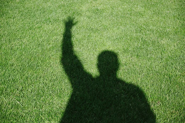 Male hand shadow silhouette with raised hand on green grass lawn background