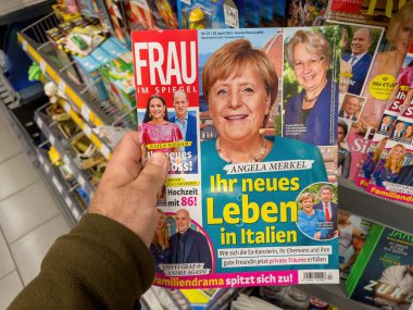 Berlin, Germany - Apr 23, 2022: Frau im Spiegel newspaper magazine at press kiosk, POV male hand holding reading the title Your new life in Italy and portrait of Angela Merkel and Joachim Sauer
