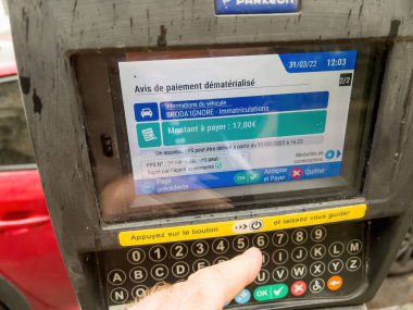 Strasbourg, France - Mar 31, 2022: POV male hand using Parkeon parking meters with digital display showing the cost of the fine for unallowed parking of 17 euros with usual price of 35