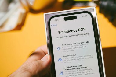 Paris, Fransa - Bölüm 17, 2022: Yeni Apple Bilgisayarlı iPhone 14 Pro akıllı telefon ile el ele tutuşan erkek acil durum imdat menüsü - kaza tespiti ve uydu aracılığıyla acil durum -