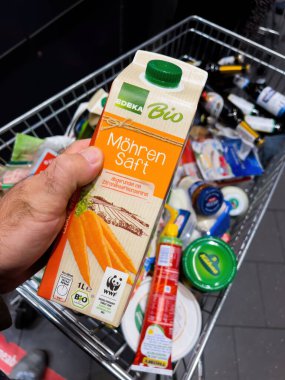 Frankfurt, Almanya - 17 Sep 2022: Mohren Saft havuç suyu ile POV erkek eli Edeka tarafından bir markette tam bir alışveriş arabası dolusu sebzenin üstünde organik olarak üretildi.