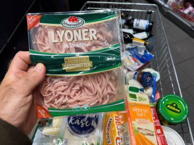 Frankfurt, Almanya - 17 Şubat 2022: Bir markette alışveriş arabasının üstündeki salata için Lyoner etiyle polis erkek eli