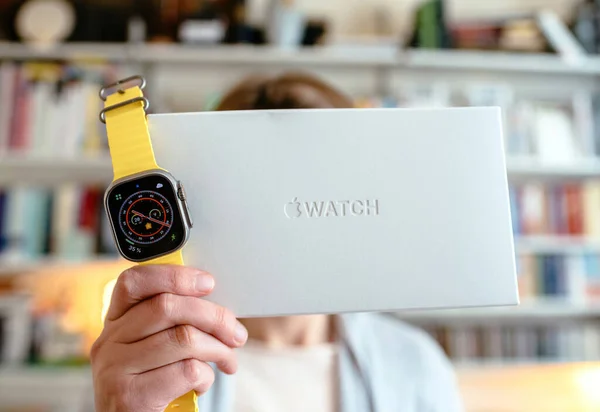 ロンドン イギリス 2022年9月28日 新しいAppleコンピュータを持つ女性Apple Watch Ultraが革新的なパッケージの隣にある バックグラウンドでリビングルームの本棚 — ストック写真