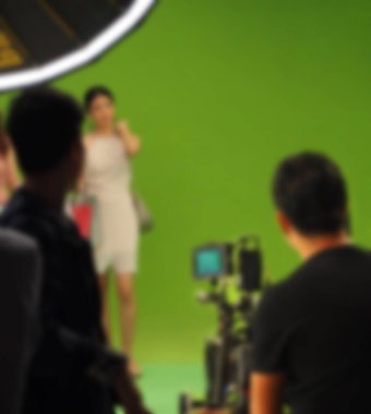 Büyük yeşil ekran arka planında televizyon reklamı videosu çekerken bulanık görüntüler. Film ekibi aktörle çalışıyor. Profesyonel dijital kamera ve ışıklandırma seti. film perde arkasında