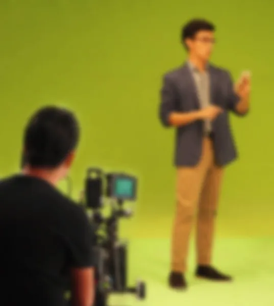 Blurry images of making TV commercial movie video in big green screen background. Film crew team working with actor. Recording by professional digital camera and lighting set. film behind the scenes