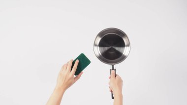 Esrar temizleme. Erkek adam beyaz arka planda bulaşık deterjanıyla tencereyi temizlerken yumuşak tarafı sarı, yemek pişirdikten sonra hijyen için sert tarafı yeşile boyuyor. Elektrikli kap.. 