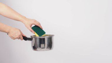 Esrar temizleme. Erkek adam beyaz arka planda bulaşık deterjanıyla tencereyi temizlerken yumuşak tarafı sarı, yemek pişirdikten sonra hijyen için sert tarafı yeşile boyuyor. Elektrikli kap.. 