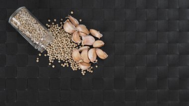 Sarımsak ve biber. Doğal sarımsaklar ve cam şişede beyaz biber, siyah arka planda tabak altlığı. Pek çok yemek tarifi için gerekli. Acı ve baharatlı sarımsak ve biberi temsil eder..