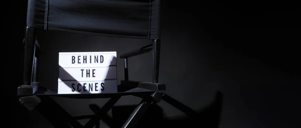 Director chair with behind the scene banner light box. Letterboard text Lightbox or Cinema Light box. Movie clapperboard and Director chair. Black Background. Represent video behind the scenes is on.