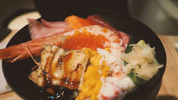 Close up images of japanese seafood rice bowl or kaisendon sashimi donburi or KAISEN CHIRASHI DON which have raw fresh ogura uni shrimp crab and fish on rice bowl. wood table from top view angle.