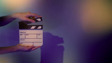 Film tahtası ya da alkışlama tahtasının bulanık görüntüleri. Stüdyoda film çekimi ya da kayıt için renk arkaplanı üzerinde el ele tutuşan boş bir film. Youtuber video üretimi için film tahtası.