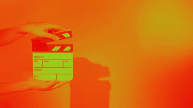 Film tahtası ya da alkışlama tahtasının bulanık görüntüleri. Stüdyoda film çekimi ya da kayıt için renk arkaplanı üzerinde el ele tutuşan boş bir film. Youtuber video üretimi için film tahtası.