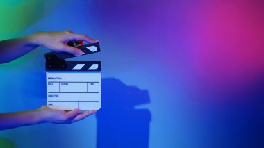 Film tahtası ya da alkışlama tahtasının bulanık görüntüleri. Stüdyoda film çekimi ya da kayıt için renk arkaplanı üzerinde el ele tutuşan boş bir film. Youtuber video üretimi için film tahtası.