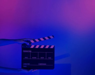Film tahtası ya da alkışlama tahtasının bulanık görüntüleri. Stüdyoda film çekimi ya da kayıt için renk arkaplanı üzerinde el ele tutuşan boş bir film. Youtuber video üretimi için film tahtası.