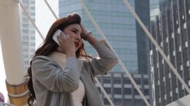 Asyalı iş kadını saatlere bakıyor ve akıllı telefondan konuşuyor. Zaman ve karamsarlık yüzünden stresliyim. Çalışan kadın ve cep telefonu. Yoğun çalışma saatlerini temsil et ve büyük şehir konseptinde çalış.