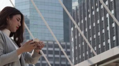 Asyalı iş kadını saatlere bakıyor ve akıllı telefondan konuşuyor. Zaman ve karamsarlık yüzünden stresliyim. Çalışan kadın ve cep telefonu. Yoğun çalışma saatlerini temsil et ve büyük şehir konseptinde çalış.