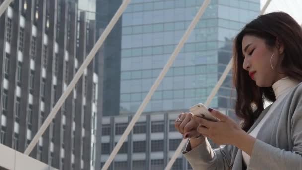 アジアの実業家は時計を見て スマートフォンで話しています 時間と気分が気になる 働く女性と携帯電話 ラッシュアワーの労働時間を表現し 大都市のコンセプトで働く — ストック動画