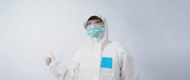 PPE takımındaki doktor beyaz lastik eldivenler ve temiz gözlükler takıyor ve yeşil N95 yüz maskesi salgın Coronavirus 'u koruyor. El işareti yap. Virüsü yenen zaferi temsil ediyor. İzole edilmiş.