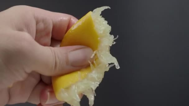 黒の背景にレモンの半分を絞る手 ライムドロップでライムを手絞る スタジオ4Kビデオ映像で手にレモン汁を押してスクワット 酸っぱくて爽やかなドリンクメニューを代表する — ストック動画