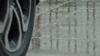 Yağmur damlaları ve yağmur suyunda araba lastikleri. Yağmurda araba park etmek. Yağmur mevsimi ve ıslak kaldırımda lastikler. Islak bir yolda araba lastiği ya da tekerlekleri kapatın. Yağmur mevsimi kavramında otomatiği temsil et.