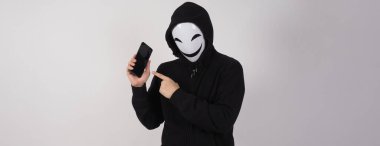 Anonim hacker ve yüz maskesi elinde akıllı telefonla. Siyah kapüşonlu tişörtlü adam beyaz arka planda cep telefonu kullanıyor. Siber suçlar veri hackleme veya kişisel veri çalma kavramını temsil et