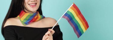 LGBTQ 'lu bir kadın mavi yeşil arka planda duran bir bayrak taşıyor. Boynunda gökkuşağı eşarbı olan Asyalı LGBTQ kadını. Zeki, neşeli ve enerjik görün. LGBTQ çeşitlilik gurur kavramı.
