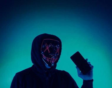 Digital security Concept. Anonymous hacker with mask holding smartphone hacked. Personal and Cyber data security in mobile phone stolen by man in mask. Represent digital privacy protection concept.