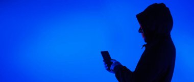 Digital security Concept. Anonymous hacker with mask holding smartphone hacked. Personal and Cyber data security in mobile phone stolen by man in mask. Represent digital privacy protection concept.