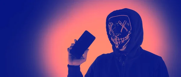 Digital security Concept. Anonymous hacker with mask holding smartphone hacked. Personal and Cyber data security in mobile phone stolen by man in mask. Represent digital privacy protection concept.