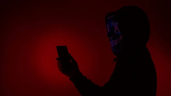 Digital security Concept. Anonymous hacker with mask holding smartphone hacked. Personal and Cyber data security in mobile phone stolen by man in mask. Represent digital privacy protection concept.