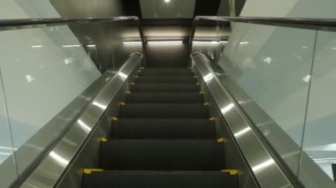 Using Escalator. Point of view or POV Video footage. Close up shot of empty moving staircase running up and down. Modern escalator stairs move indoors going up and down. Escalator with glass sides.