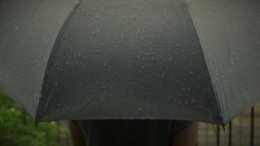 Gri şemsiyeye yağmur yağıyor. Bangkok 'ta akşam yağmurunda gümüş şemsiye. Şemsiyeye düşen yağmur damlaları. Kötü kış yağmurlu mevsimi ya da korunmayı temsil ediyor. Yağmurda insan ve şemsiye.