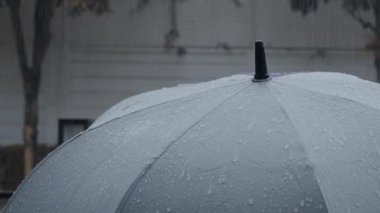 Gri şemsiyeye yağmur yağıyor. Bangkok 'ta akşam yağmurunda gümüş şemsiye. Şemsiyeye düşen yağmur damlaları. Kötü kış yağmurlu mevsimi ya da korunmayı temsil ediyor. Yağmurda insan ve şemsiye.